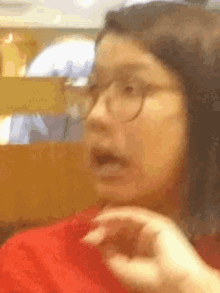 a woman wearing glasses and a red shirt is making a surprised face