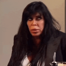 a woman with long black hair is sitting at a table with a spoon in her hand .