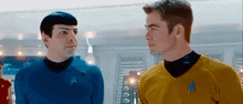 two men in star trek uniforms are standing next to each other looking at each other .
