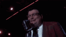 a man in a red jacket is singing into a microphone in a dark room