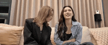 two women are sitting on a couch talking to each other and smiling .