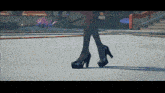 a woman wearing black high heels is walking on a concrete surface