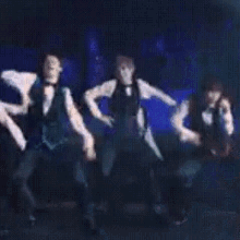 a group of men in tuxedos are dancing on a stage in a dark room .