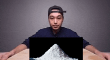 a man wearing a baseball cap is sitting at a table with a pile of white powder .