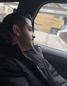 a man in a black jacket is sitting in a car looking out the window