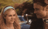 a man and a woman are looking at each other with a car in the background