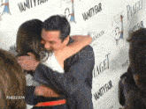 a man and a woman hugging in front of a wall that says vanity fair