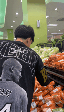 a man wearing a kobe jersey stands in front of carrots in a grocery store