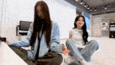 two girls are sitting on the floor with one wearing a white t-shirt that says ' a.r. ' on it