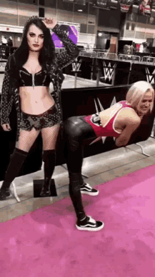 two women are standing next to each other on a pink carpet in front of a wwe sign .