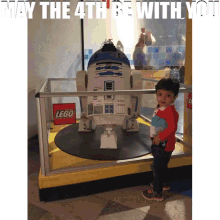 a little boy stands in front of a lego r2d2 model