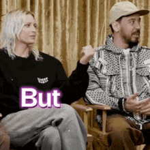 a man and a woman are sitting next to each other and the woman is wearing a black sweater that says but