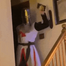 a person dressed as a crusader is standing in a hallway next to a staircase holding a sword .
