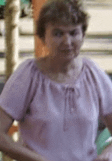 a woman in a pink shirt is standing in front of a staircase and smiling .