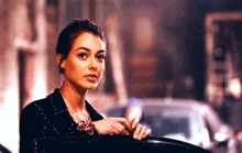 a woman in a black jacket is standing next to a car