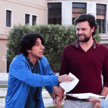 a man in a blue jacket is shaking hands with another man in a red shirt