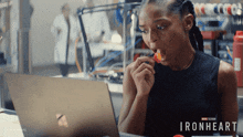a woman eating a tomato in front of a laptop with the word ironheart on it