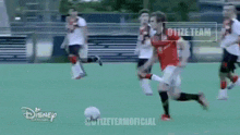 a man in a red shirt is kicking a soccer ball while another man in a white shirt tries to stop him .