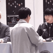 a man in a black leather jacket is talking to another man in a white jacket .