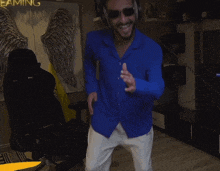 a man in a blue shirt and white pants is dancing in front of a sign that says gaming