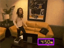 a woman is dancing in a living room with a clock reading 4:50 pm