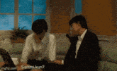 two men are sitting on a couch talking to each other while using a laptop computer .