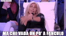 a woman is sitting in a chair with a microphone in her hand and says ma che vada un po ' a fanculo
