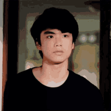 a young man in a black shirt is looking at the camera .