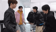 a group of young men are standing in a room and one of them is wearing a jacket that says supreme on it