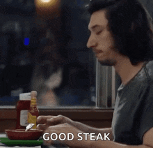 a man is sitting at a table with a bowl of ketchup and a plate of food and the word good steak is on the table