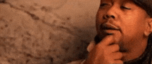 a man with a beard is holding his hand to his chin and thinking .