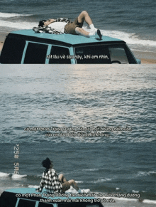 a man is laying on the roof of a blue van on the beach