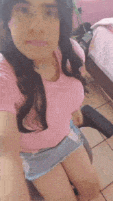 a woman in a pink shirt and shorts is taking a selfie while sitting in a chair .
