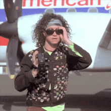 a man wearing sunglasses holds a camera in front of an american airlines airplane