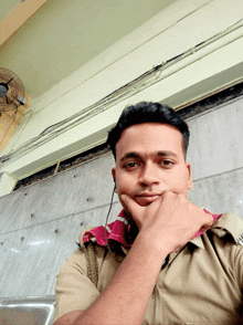 a man with his hand on his chin in front of a wall and a fan