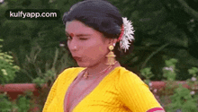 a woman in a yellow top and earrings is standing in a garden .