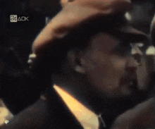 a man in a hat is talking to a group of people with the letters 24 ack in the corner