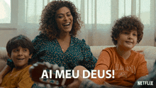 a woman sits on a couch with two boys and the words ai meu deus above her