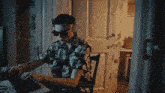 a man wearing sunglasses and a hawaiian shirt is typing on a laptop