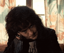a man with long hair is talking on a cell phone while wearing a leather jacket .