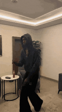 a person in a hooded sweatshirt is dancing in a living room