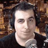 a man wearing headphones stands in front of a microphone and looks at the camera