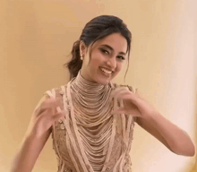 a woman wearing a very long necklace is smiling and making a heart with her hands