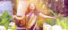 a woman in a saree is dancing with her arms outstretched in a garden .