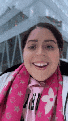 a woman wearing a pink scarf and a louis vuitton shirt smiles for the camera