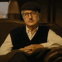 a man wearing glasses and a hat sits on a chair