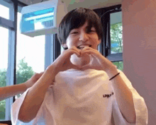 a young man is making a heart shape with his hands while wearing a white shirt .
