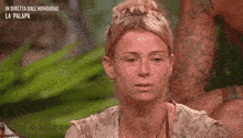 a woman is sitting at a table with a man in the background and making a funny face .