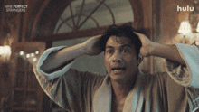 a man in a bathrobe is looking at his hair with the hulu logo behind him