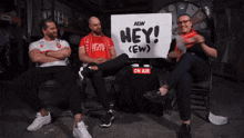 three men are sitting in front of a sign that says hey ( ew )